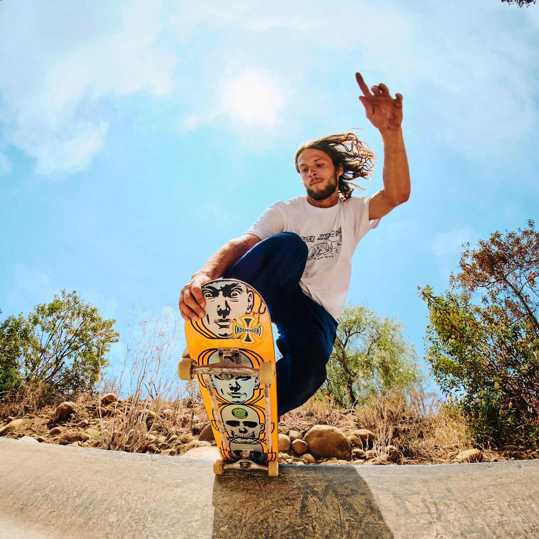 Ace Pelka skating a concrete bowl lip on a yellow skull-graphic board under a bright blue sky