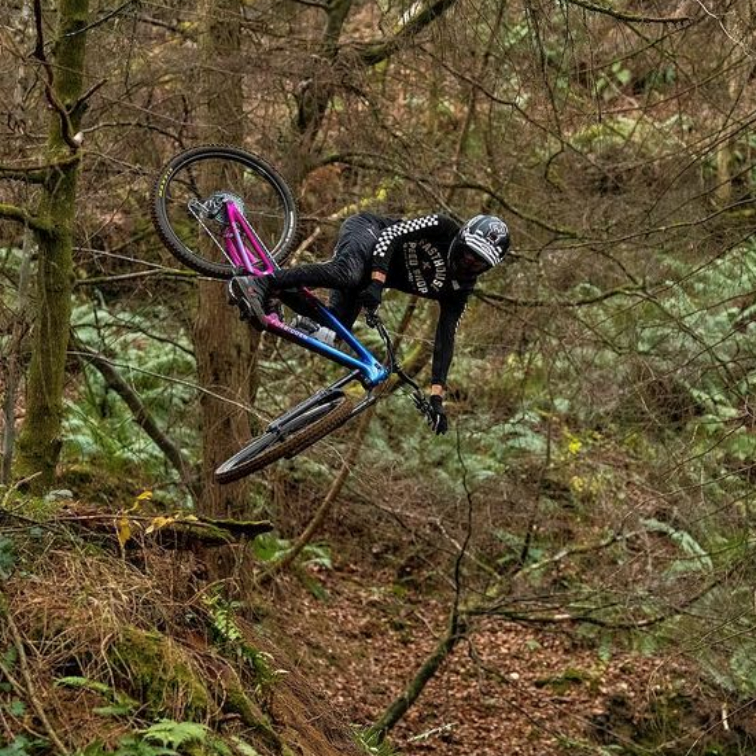 Alex Storr whipping a mountain bike sideways in the air through a mossy forest
