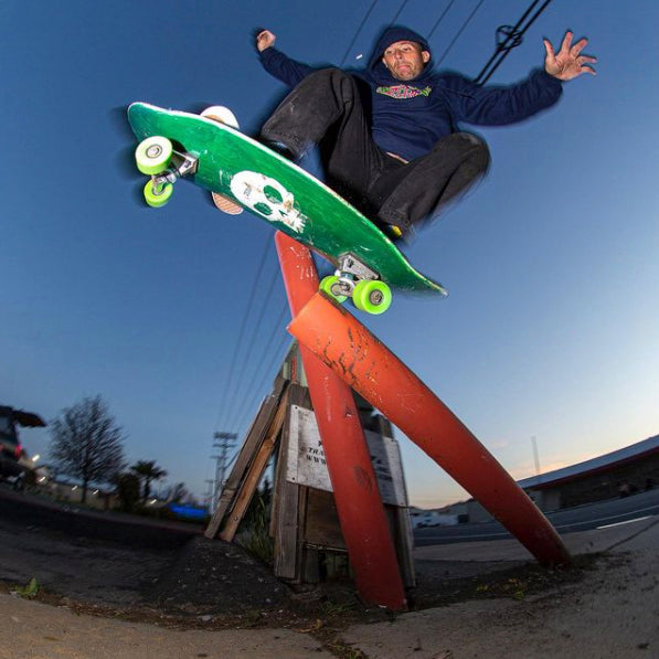 Dane Burman ollieing over an orange wooden barricade on a green skateboard at dusk
