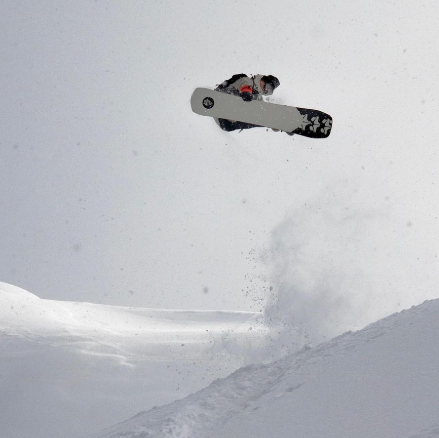 Hunter Knoll launching a snowboard jump over a powder slope, kicking up a spray of snow