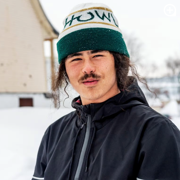 Portrait of Jacob Krugmire in a green and white "Howl" beanie and black jacket on a snowy street