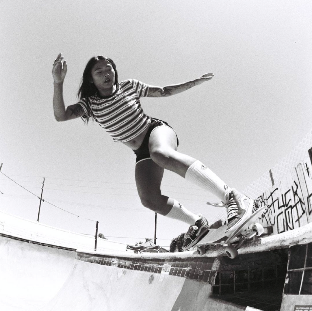 Black-and-white shot of Janthavy Norton skating a pool coping in a striped tee and tube socks