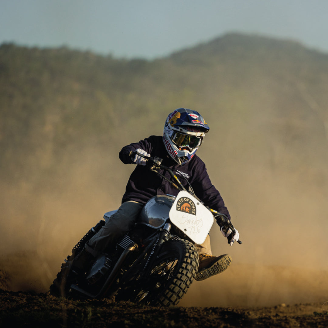 Kelana Humphrey riding a dirt bike through a cloud of dust, wearing a full-face helmet and goggles