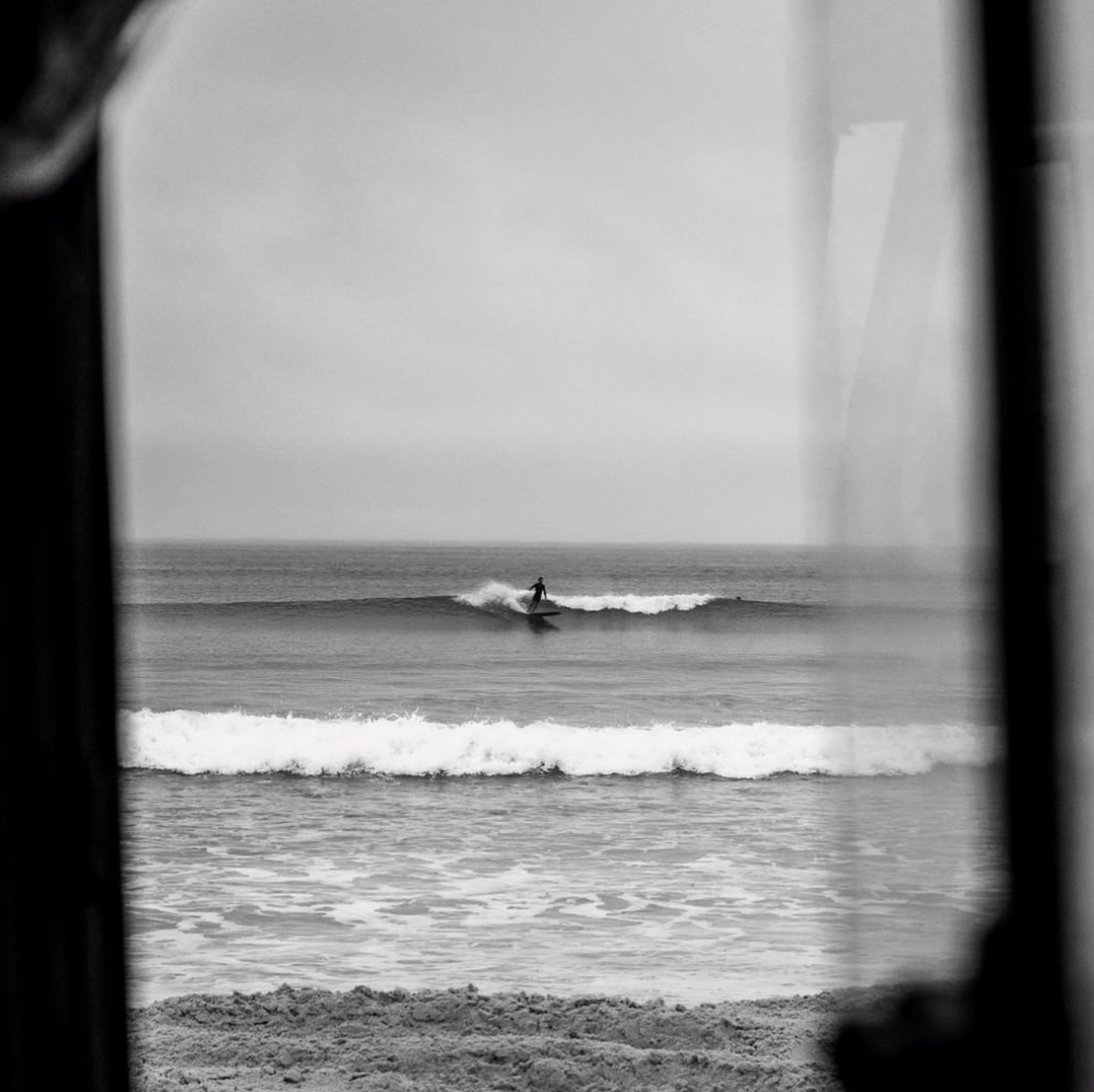 Matt Cuddihy: black-and-white view through a window of a lone surfer riding a wave