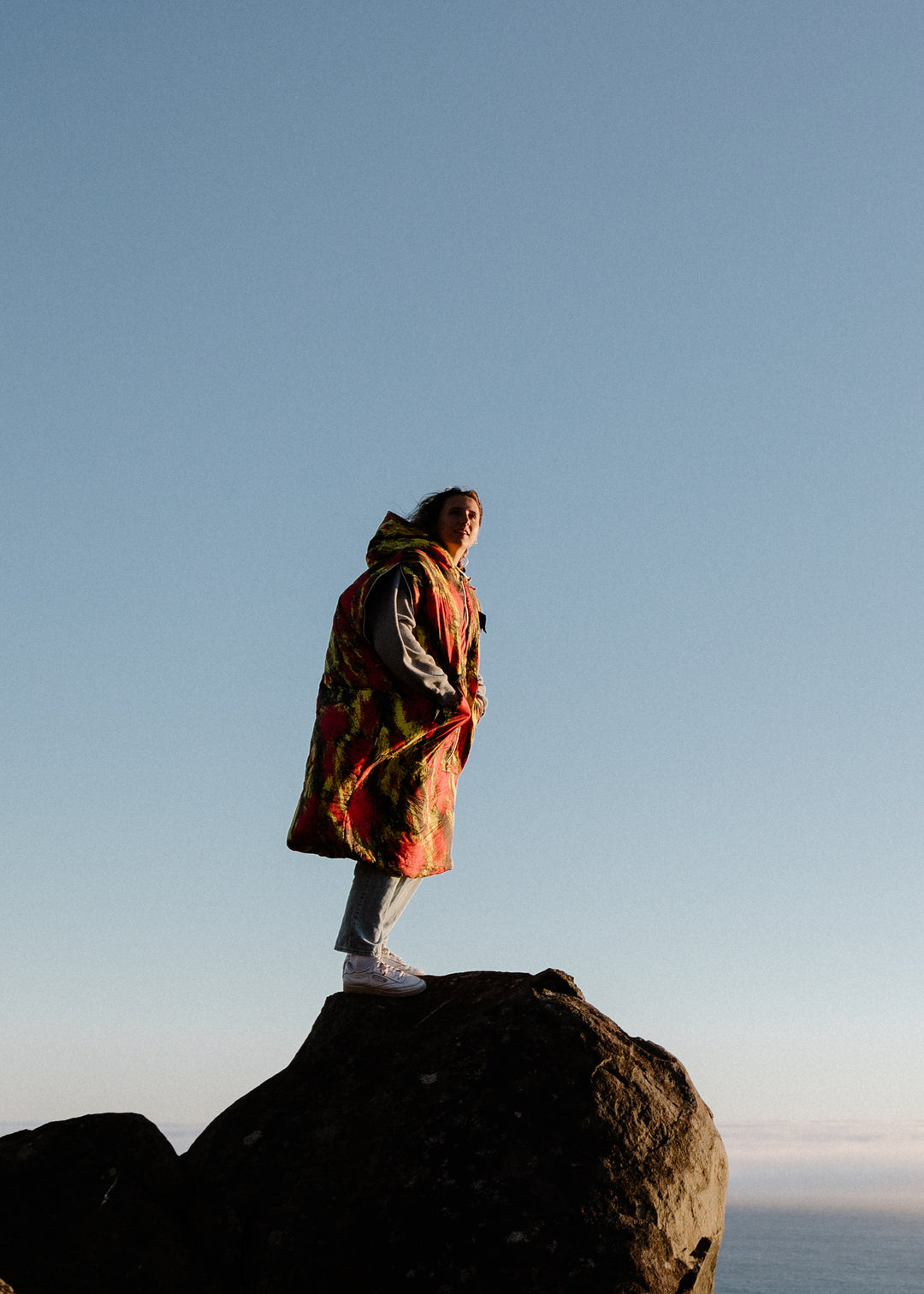 Woman in a red and yellow print Napsack standing on a boulder against a clear blue sky
