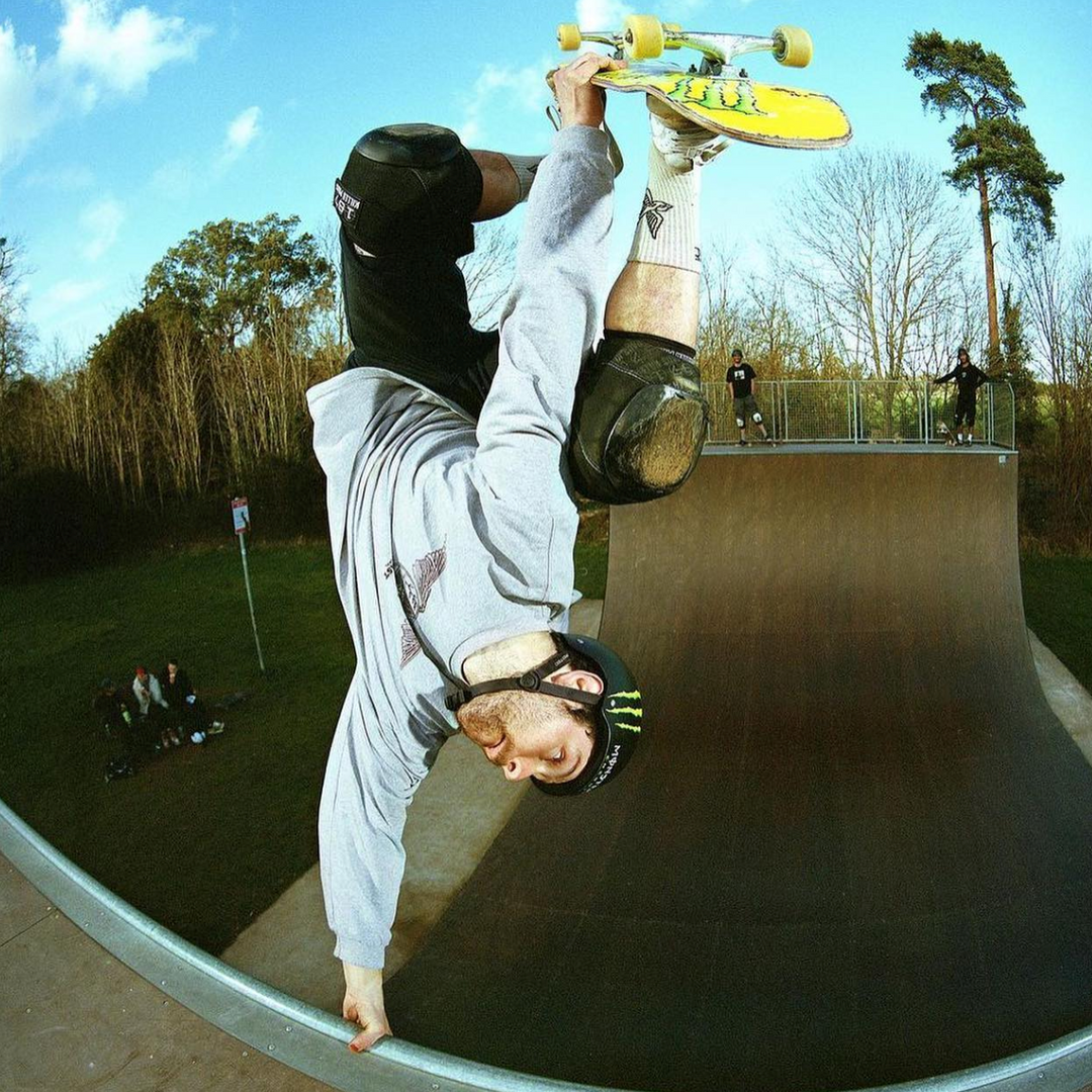 Sam Beckett doing a handplant on a halfpipe coping in a gray hoodie and helmet