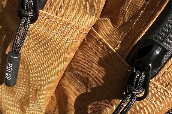 Close-up of a tan ripstop Poler bag with black zipper pulls and a Poler-branded cord lock