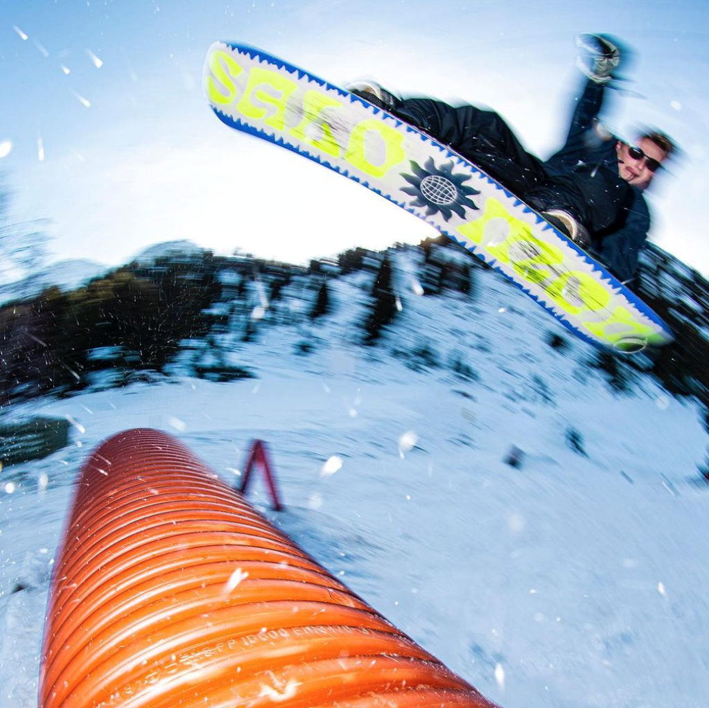 Will Smith flying sideways on a snowboard over an orange tube rail on a sunny slope