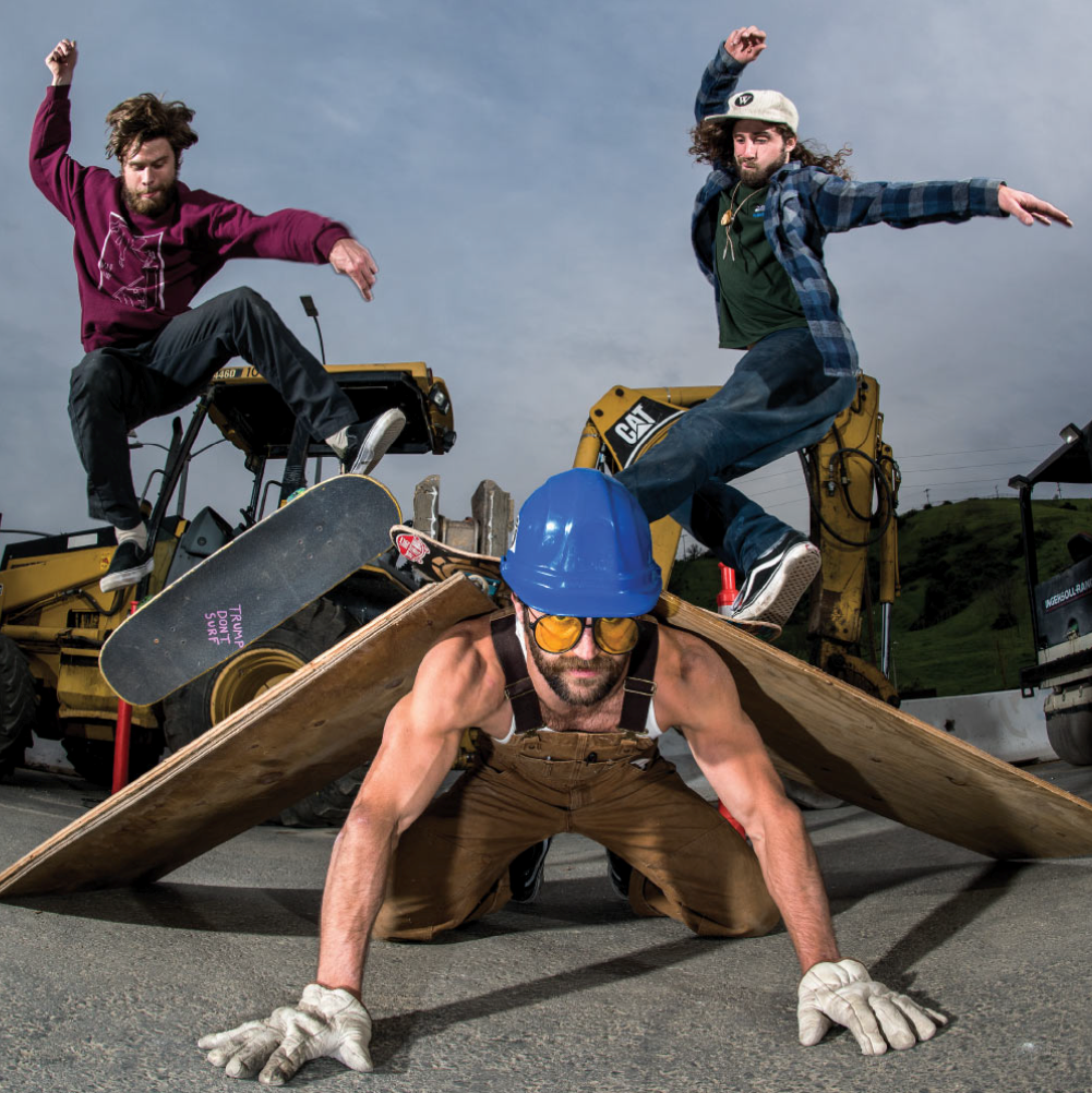 Worble crew: two skaters jumping over a man in a hard hat holding up wooden ramps by construction equipment