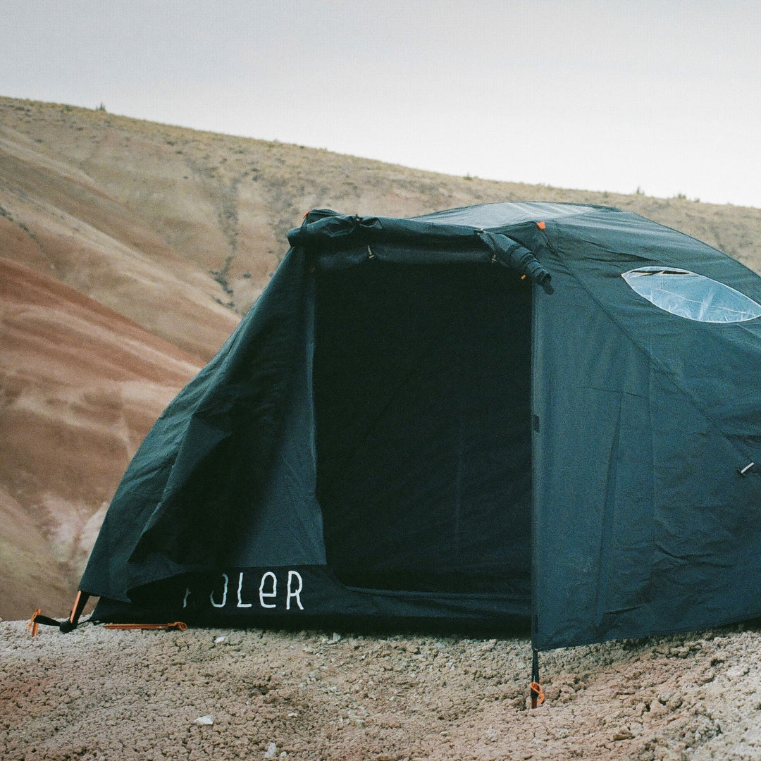 Dark green Poler tent with a clear skylight window pitched on a ridge above red-striped desert hills