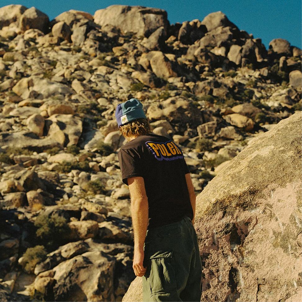 Person in a navy beanie and black Poler logo tee looking out over a boulder-strewn desert hillside