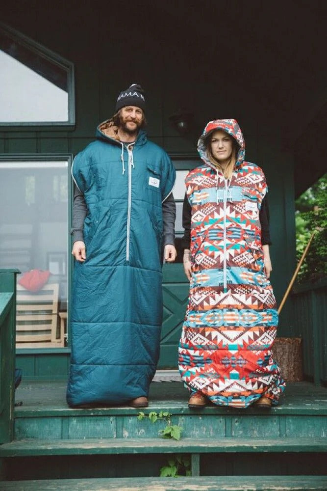 Man in a teal Napsack and woman in a patterned Napsack standing side by side on a cabin porch