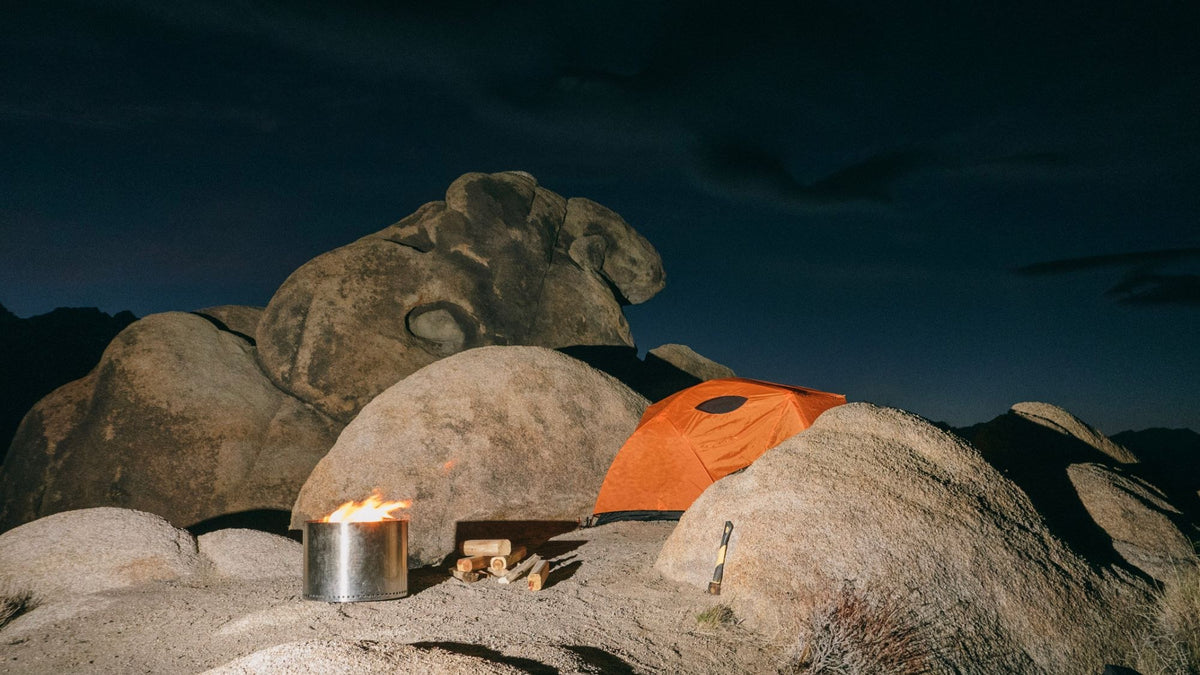 Orange tent and campfire among boulders at night