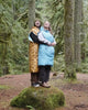 Couple in Napsacks hugging atop a mossy boulder in an old-growth forest