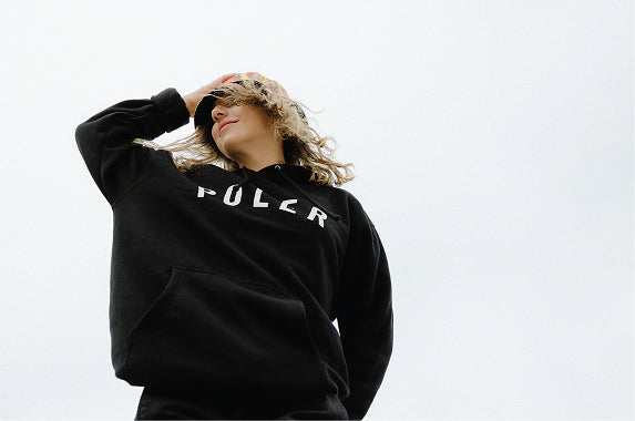 Woman in a black Poler logo hoodie against an overcast sky